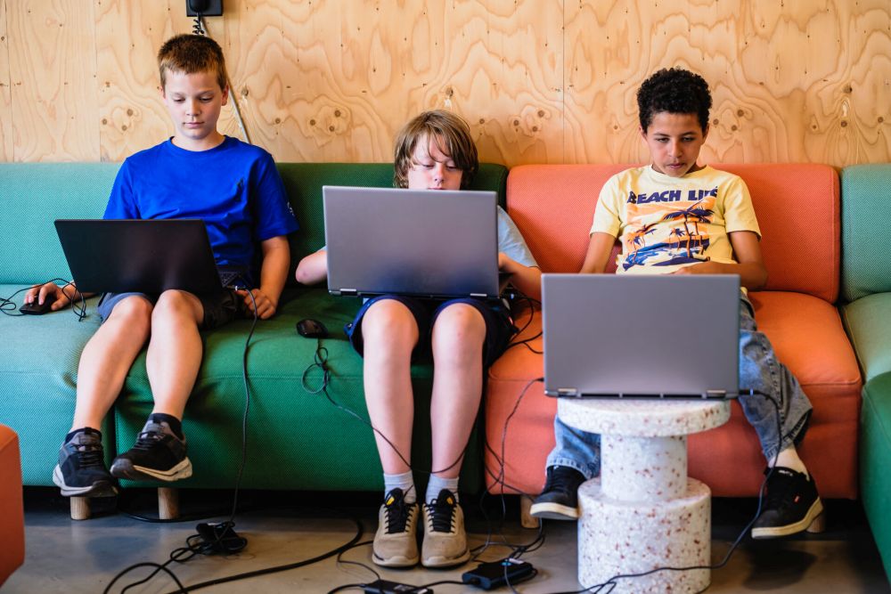 Drei Jugendliche sitzen auf einem Sofa und arbeiten an Laptops.